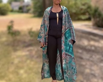 May include: A long, flowing green and brown tie-dye kimono with a black top and pants underneath. The kimono has a loose fit and is made of a soft, flowing fabric.