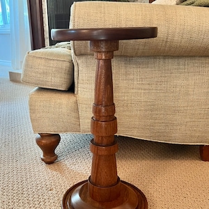 May include: A dark brown wooden end table with a round top and a pedestal base. The base is made of stacked rings of wood.