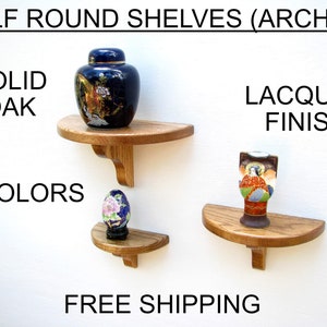 May include: Two half-round wooden shelves with decorative brackets. The shelves are made of solid oak and have a lacquer finish. The shelves are displayed on a white wall with decorative items on top. The text "HALF ROUND SHELVES (ARCHES)", "SOLID OAK", "9 COLORS", "LACQUER FINISH", and "FREE SHIPPING" is visible on the image.