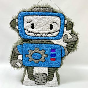 May include: A blue and gray robot pinata with a white face and a gear on its chest. The pinata has a loop at the top for hanging.