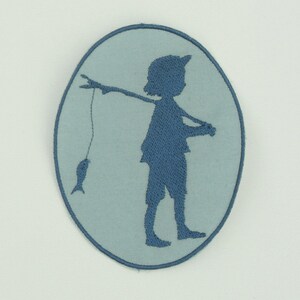 Könnte beinhalten: Ein blauer gestickter Aufnäher mit einem Kind, das eine Angelrute mit einem Fisch an der Leine hält. Der Aufnäher ist auf einem hellblauen Hintergrund.