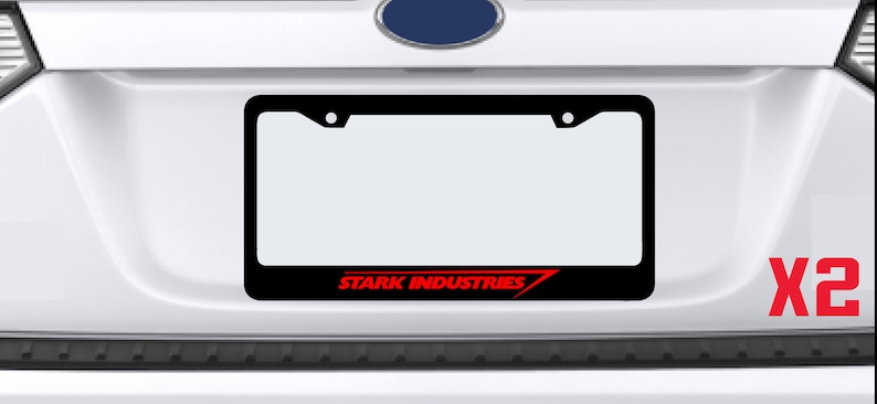 Puede incluir: Marco de matr&iacute;cula negro con un logotipo rojo de "STARK INDUSTRIES". El marco est&aacute; fijado a un coche blanco. El texto "X2" es visible en rojo en el coche.