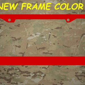 Puede incluir: Un marco de matr&iacute;cula de metal rojo con dos agujeros en la parte superior. El marco est&aacute; sobre un fondo de camuflaje. "NEW FRAME COLOR" est&aacute; escrito en amarillo en la parte superior de la imagen.