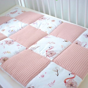Könnte beinhalten: Eine rosa-weiße Babydecke mit Patchwork-Muster mit Flamingos, Blumen und Blättern. Die Decke ist aus weichem, gestepptem Stoff und perfekt für ein Kinderzimmer.