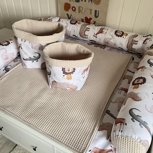 May include: Two beige waffle-weave storage baskets with animal print designs, a beige waffle-weave changing mat, and a white and beige changing pad with animal print designs.