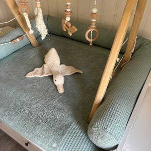 Op de afbeelding: Een houten baby-speelgym met een groene wafelstructuur speelmat en een pluche eendenspeelgoed. De gym heeft meerdere houten ringen en hangende speelgoed met kralen en kwastjes.