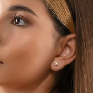 May include: A woman with long brown hair and a light brown complexion is looking up and to the right. She is wearing a light brown top and has a small diamond earring in her left ear.