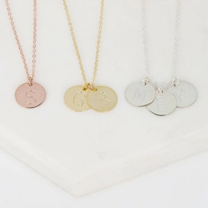 May include: Three gold necklaces with initial charms. The first necklace has a single charm with the letter "S". The second necklace has two charms with the letters "G" and "R". The third necklace has three charms with the letters "M", "E", and "V".