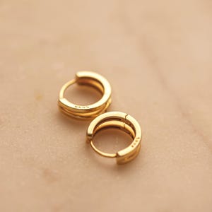 May include: A pair of gold hoop earrings with a double band design. The earrings are made of metal and have a polished finish.