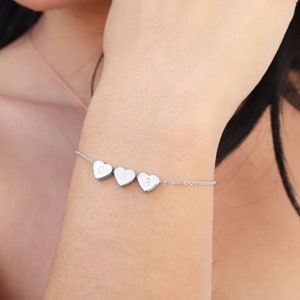 May include: A silver chain bracelet with four small heart charms, each with a letter engraved on it. The letters spell out "CIR".
