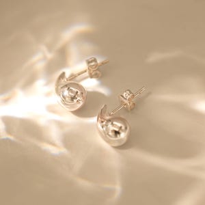 May include: A pair of silver earrings with a unique, organic shape. The earrings are made of smooth, rounded metal and have a modern, minimalist design.