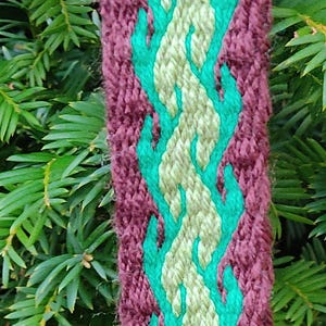 May include: Close-up of a woven textile with a central design. The textile features a burgundy background with a central pattern of light green and teal flame-like shapes. The text "Astridas Atelier" is visible.