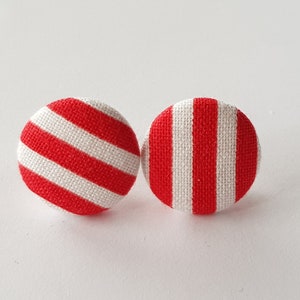 May include: A pair of red and white striped fabric earrings. The earrings are round and have a simple design.