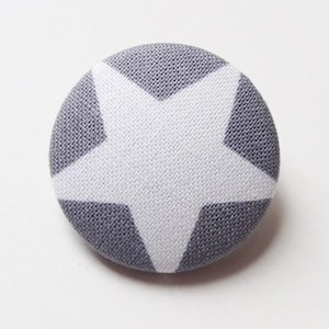 Può includere: Un bottone in tessuto grigio con un motivo a stella bianca.