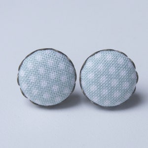 May include: A pair of light blue fabric earrings with a white polka dot pattern. The earrings have a silver metal rim.
