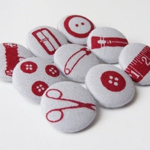 May include: Nine gray fabric buttons with red embroidery of sewing-related items, including a zipper, scissors, a measuring tape, a button, a lipstick, a bobby pin, and a sewing needle.