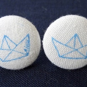 May include: Two white fabric buttons with blue embroidered origami paper boat designs.