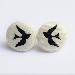 May include: A pair of white fabric button earrings with a black silhouette of a bird on each button.