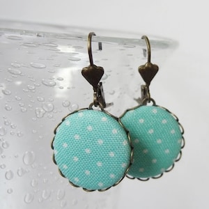 May include: A pair of turquoise blue earrings with white polka dots. The earrings are made of fabric and have a bronze metal frame.