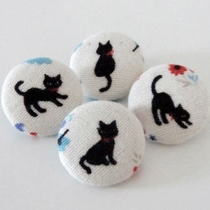 May include: Four white fabric buttons with black cat designs. Each button features a different cat pose and a white background with small blue and red floral patterns.