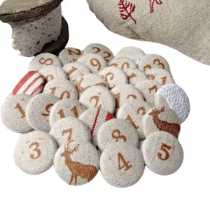 Pode incluir: Uma coleção de círculos de tecido bege, cada um com um número castanho, dispostos em grupo. Alguns círculos apresentam uma ilustração de veado castanho. Os círculos fazem parte de um calendário do Advento.