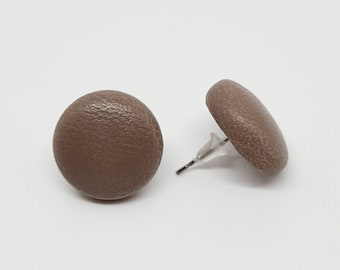 Könnte beinhalten: Ein Paar braune runde Ohrstecker. Die Ohrringe sind aus einem strukturierten Material gefertigt und haben einen silbernen Stift.