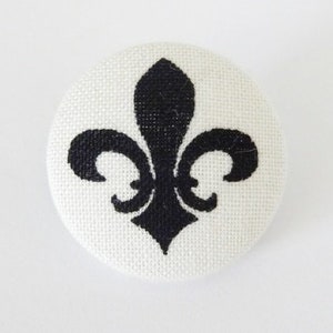 Pode incluir: Um botão branco com um design de flor-de-lis preto.