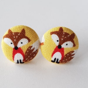 May include: A pair of yellow fabric button earrings with a fox design. The foxes are brown with red noses and white eyes.