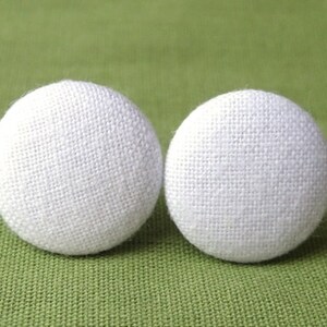 Könnte beinhalten: Zwei weiße, stoffbezogene Knöpfe. Die Knöpfe sind rund und haben eine strukturierte Oberfläche.