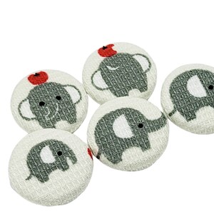 May include: Six white fabric buttons with grey elephant designs. Two of the elephants have a red apple on their head.