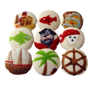 Op de afbeelding: Set van negen stoffen knopen met een piraten thema. De knopen hebben afbeeldingen van een schatkist, een vis, een piraat, een schedel en gekruiste beenderen, een palmboom, een schip en een stuurwiel.