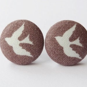 Peut inclure: Une paire de boucles d'oreilles en tissu marron avec un motif de silhouette d'oiseau blanc.