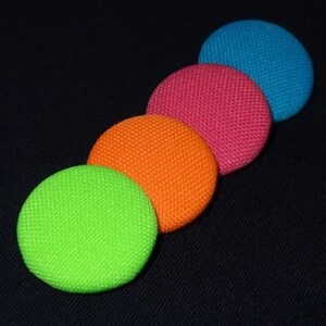 Puede incluir: Cuatro botones redondos de tela en colores brillantes: turquesa, rosa, naranja y verde.