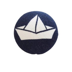 Może przedstawiać: Guzik z tkaniny w kolorze granatowym z wzorem białego papierowego statku.