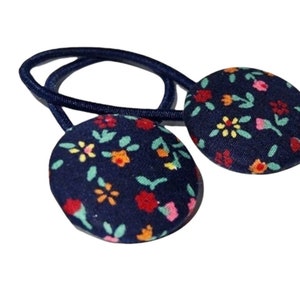 May include: Two navy blue hair ties with floral fabric covered buttons. The buttons have a white background with small red, orange, yellow, and green flowers.