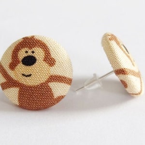 Peut inclure: Une paire de boucles d'oreilles clous en tissu marron et crème avec un motif de singe de dessin animé.