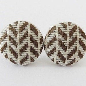 Może przedstawiać: Para kolczyków z guzików z tkaniny w brązowo-białym wzorze. Guziki są okrągłe i mają tkany wzór.