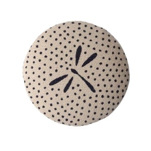 Può includere: Un cuscino rotondo beige con un motivo a pois neri e bianchi e un design a riccio di mare stilizzato nero al centro.