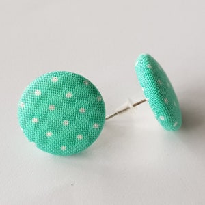 May include: A pair of teal blue fabric earrings with white polka dots. The earrings are round and have a post back.