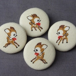 Op de afbeelding: Vier witte stoffen knopen met een bruin en wit hert ontwerp. Elke knop heeft een hert met een rode strik.