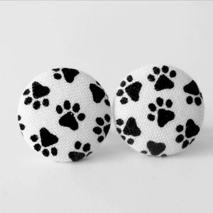 May include: A pair of white button earrings with a black paw print pattern.