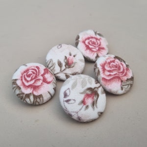 Peut inclure: Cinq boutons recouverts de tissu avec un motif floral. Les boutons présentent des roses roses et des feuilles brunes sur un fond blanc.