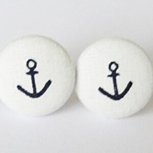 Może przedstawiać: Para białych kolczyków z guzikiem z czarnym wzorem kotwicy.