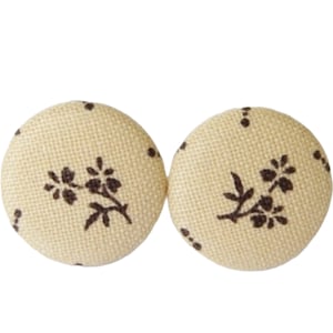 Könnte beinhalten: Zwei cremefarbene Stoffknöpfe mit braunem Blumenmuster.