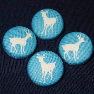 May include: Four blue fabric buttons with white deer silhouettes. The deer are facing different directions.