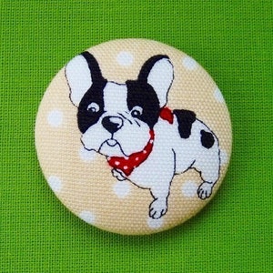 Peut inclure: Un bouton rond avec une illustration de bouledogue français. Le chien est noir et blanc avec un foulard rouge à pois. Le bouton a un fond beige avec des pois blancs, sur un fond vert.