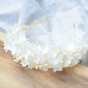 Op de afbeelding: Een witte bloemenband van gedroogde hortensia's. De band ligt op een houten oppervlak.