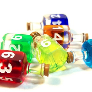 May include: Six colourful glass bottles with cork stoppers and white numbers on the sides. The bottles are filled with different coloured liquids and are lying on a white surface.