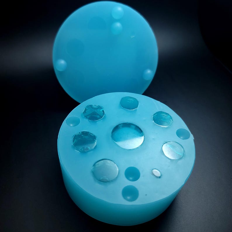 May include: A light blue silicone mold with multiple circular depressions of varying sizes. The mold is designed for creating resin jewelry or other crafts.