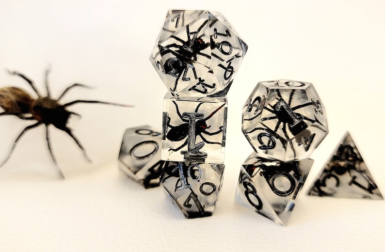 May include: A set of six clear dice with black numbers and a spider encased in each die. The dice are a d4, d6, d8, d10, d12, and d20.